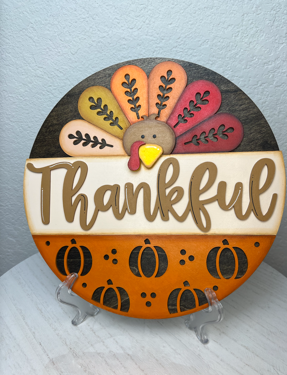 Decorative plate with a turkey design and 'Thankful' text on a stand against a light blue background.