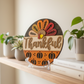 Decorative sign with a turkey design and 'Thankful' text on a shelf.