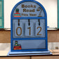 Souvenir Design Books Read This Year wooden counter in blue, number tiles showing 012, with a coffee cup and stacked books on the bottom shelf