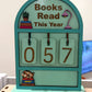 Souvenir Design Books Read This Year wooden counter in mint green, number tiles showing 057 and a calico cat on stacked books
