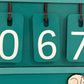 Close-up of the hanging number tiles on a turquoise Souvenir Design book counter showing 067