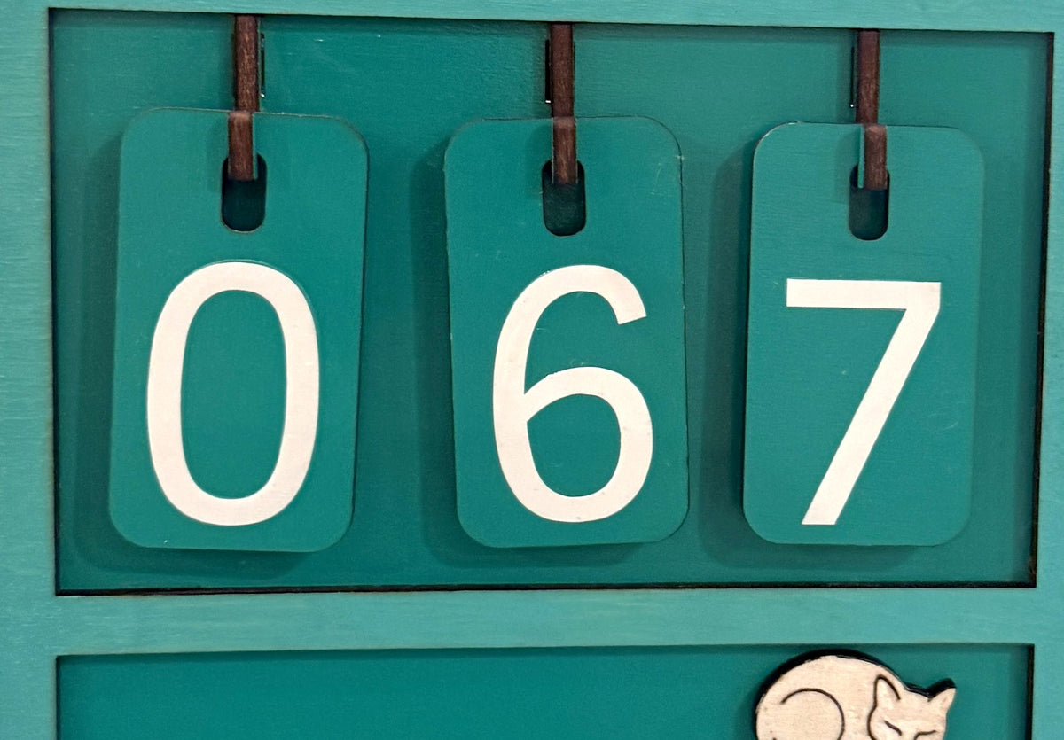 Close-up of the hanging number tiles on a turquoise Souvenir Design book counter showing 067