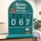 Souvenir Design Books Read This Year wooden counter in turquoise with white numbers showing 067 and a sleeping cat on stacked books