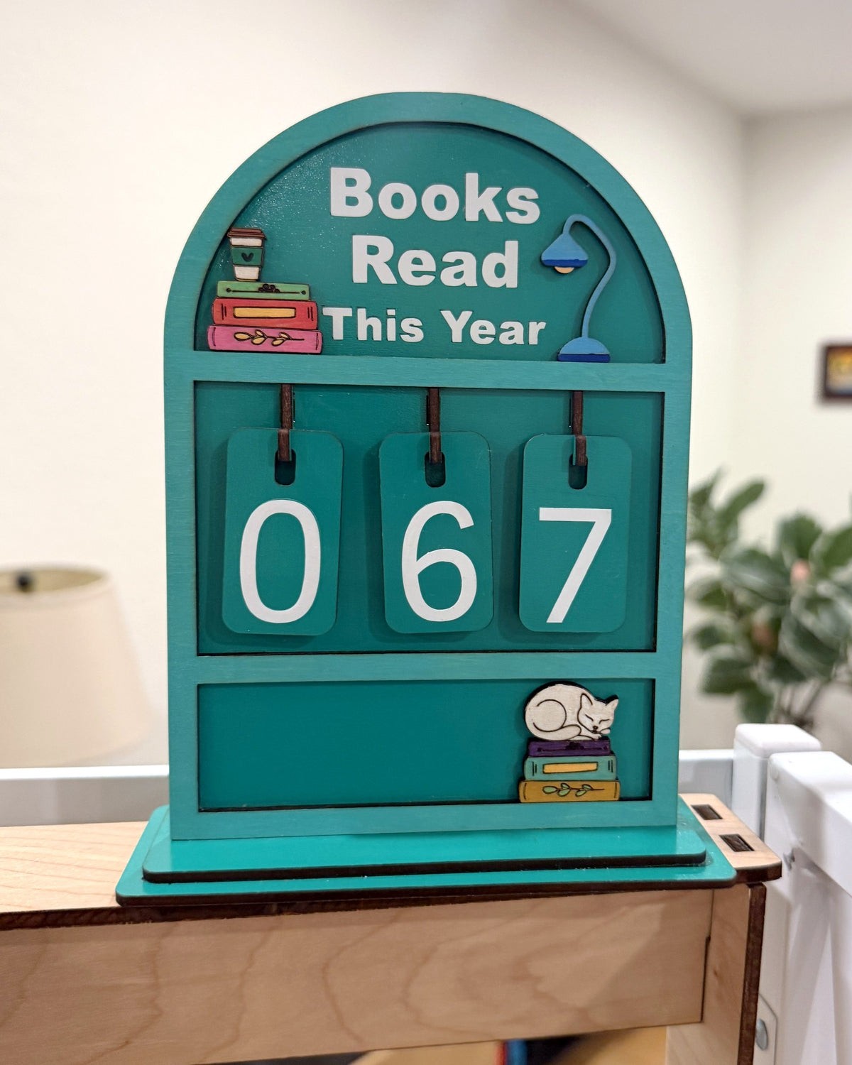 Souvenir Design Books Read This Year wooden counter in turquoise with white numbers showing 067 and a sleeping cat on stacked books