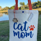 Tote bag with 'Cat Mom' text and paw print design, held by a person outdoors.