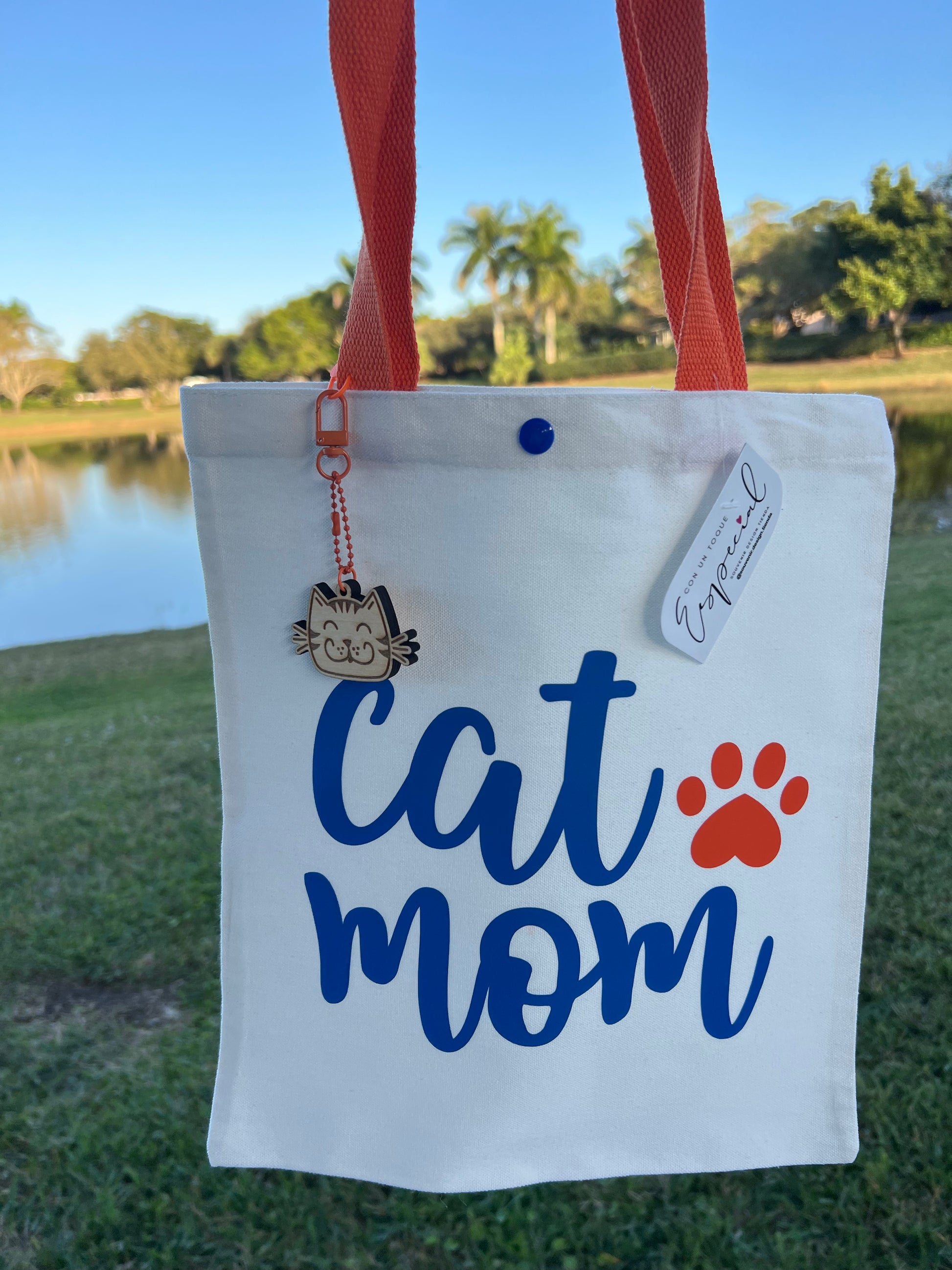 Tote bag with 'Cat Mom' text and paw print design, held by a person outdoors.