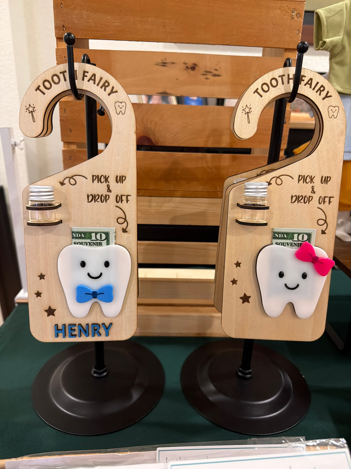 Two wooden Tooth Fairy door hangers by Souvenir Design, each with a small jar for the tooth and a smiling tooth holding a bill, one with the name HENRY in raised blue letters