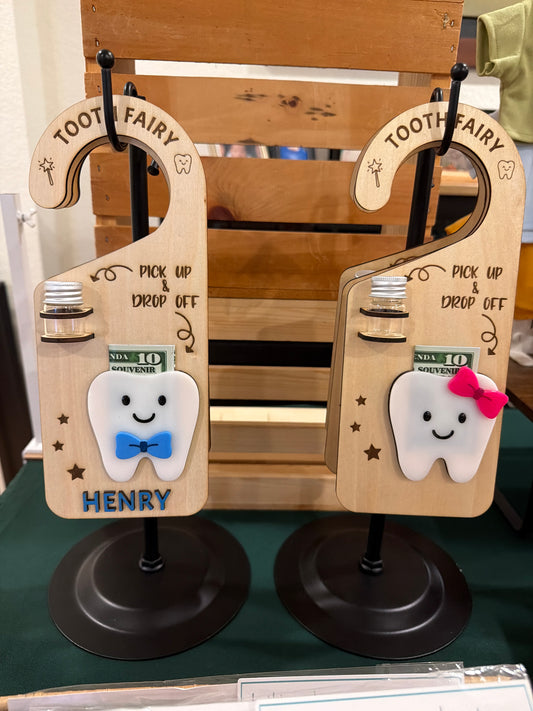 Two wooden Tooth Fairy door hangers by Souvenir Design, each with a small jar for the tooth and a smiling tooth holding a bill, one with the name HENRY in raised blue letters