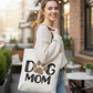 Woman holding a tote bag with 'Dog Mom' text in an outdoor setting