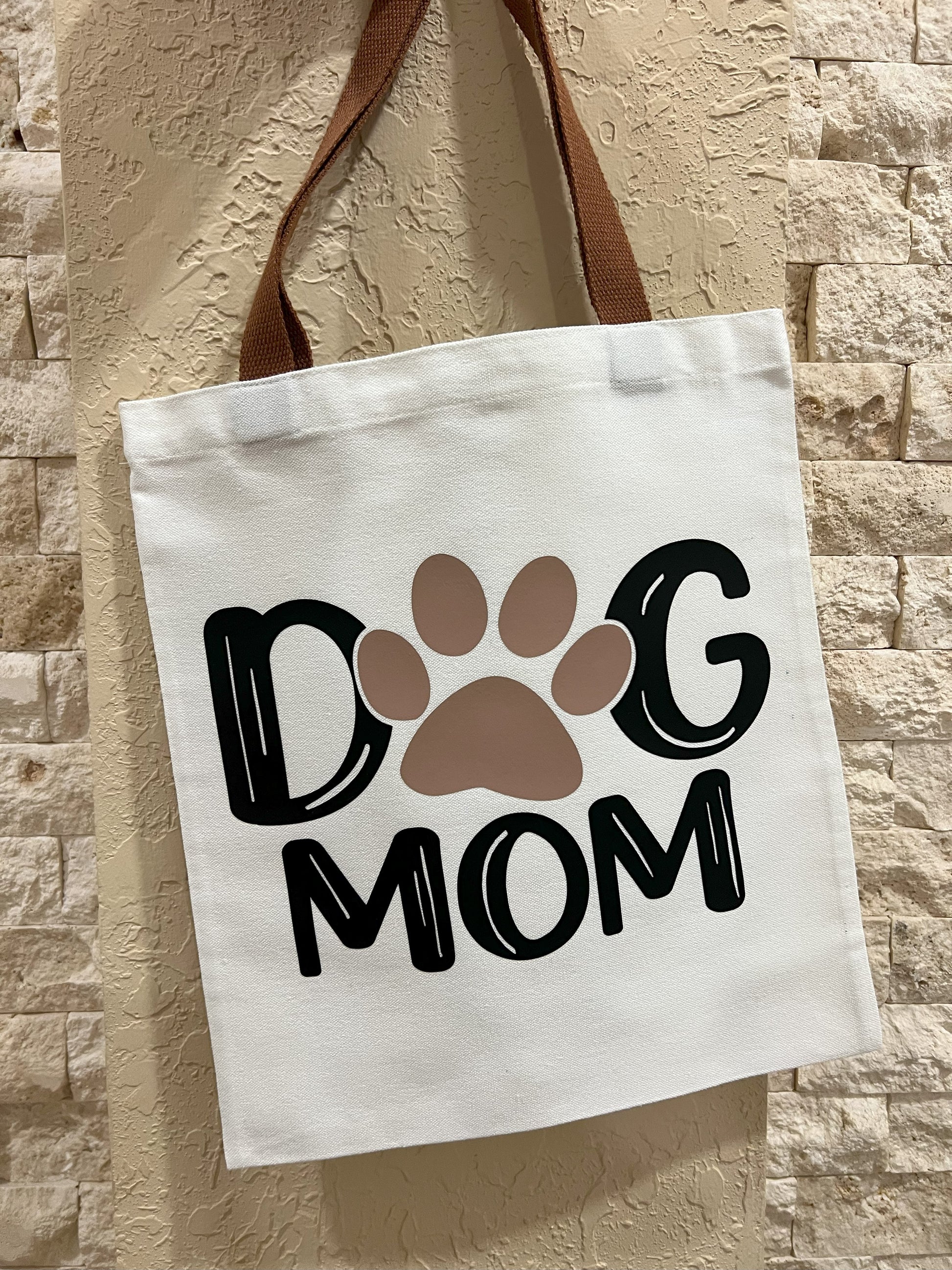 Tote bag with 'Dog Mom' text and paw print design against a stone wall background