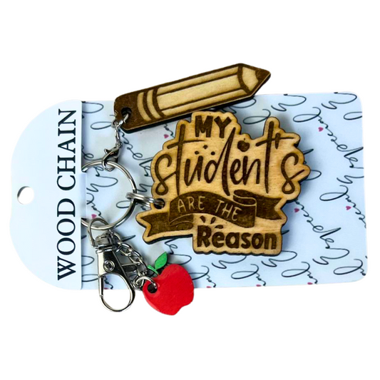Engraved wood teacher keychain "My Students Are the Reason" with pencil and red apple charms on a card, by Souvenir Design