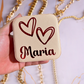 Gold square jewelry box with 'Maria' and heart designs held by a hand against a marble background.