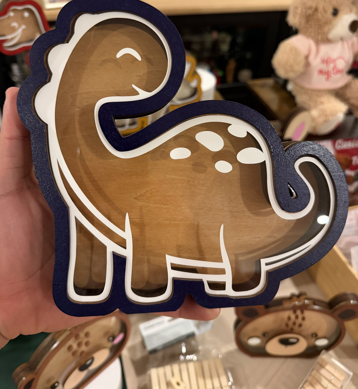 Souvenir Design hand-painted wooden dinosaur piggy bank with a clear front, navy blue and white outline, held in one hand