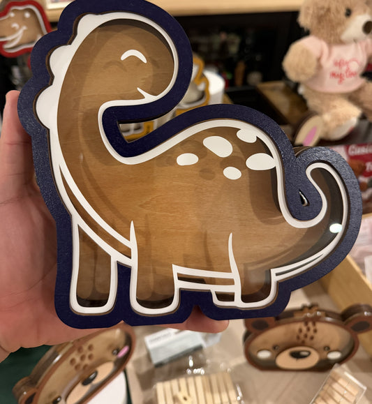 Souvenir Design hand-painted wooden dinosaur piggy bank with a clear front, navy blue and white outline, held in one hand