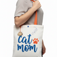 Person holding a tote bag with 'Cat Mom' text and paw print design.