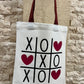Tote bag with tic-tac-toe design and hearts against a stone wall background