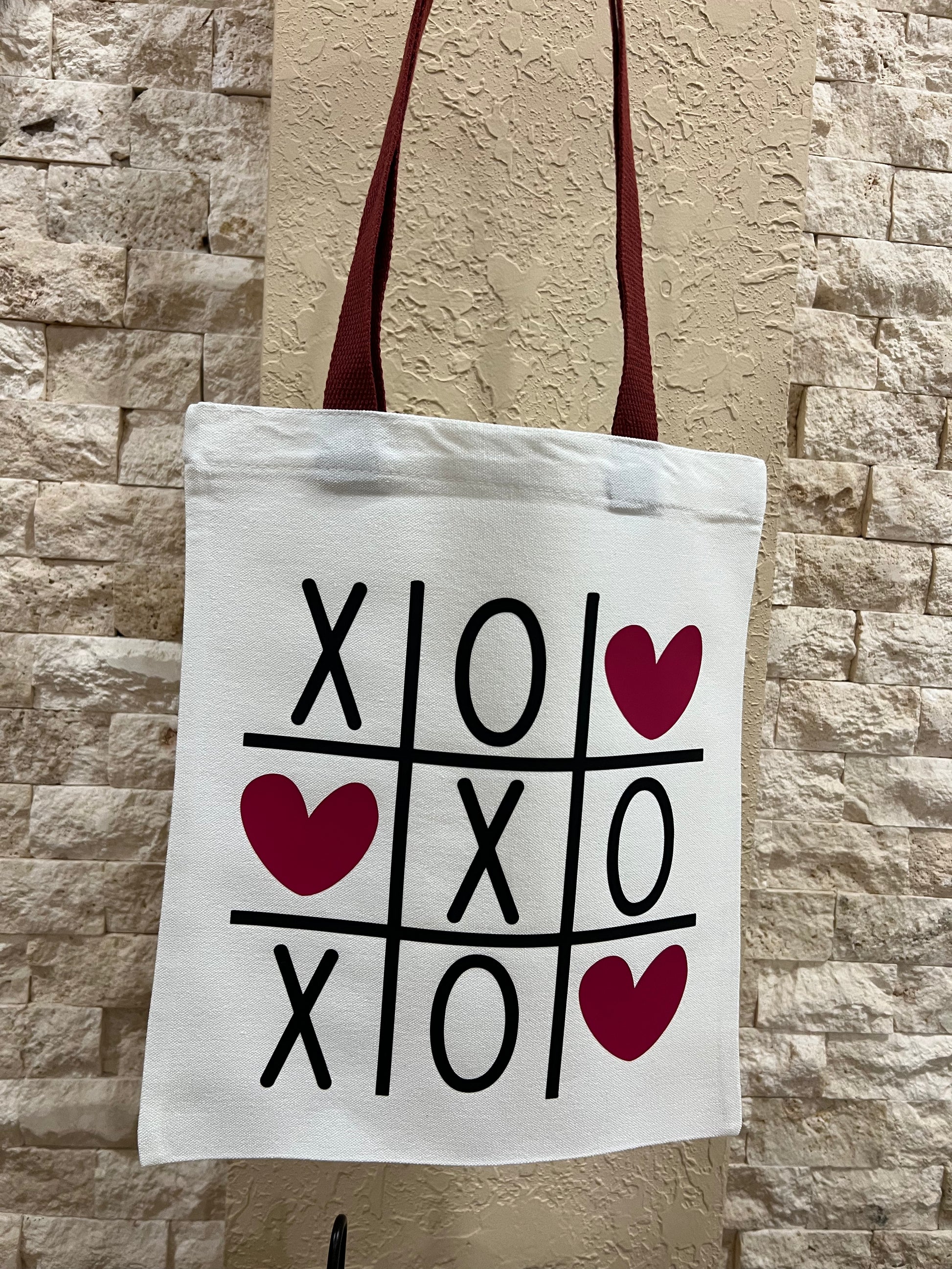 Tote bag with tic-tac-toe design and hearts against a stone wall background